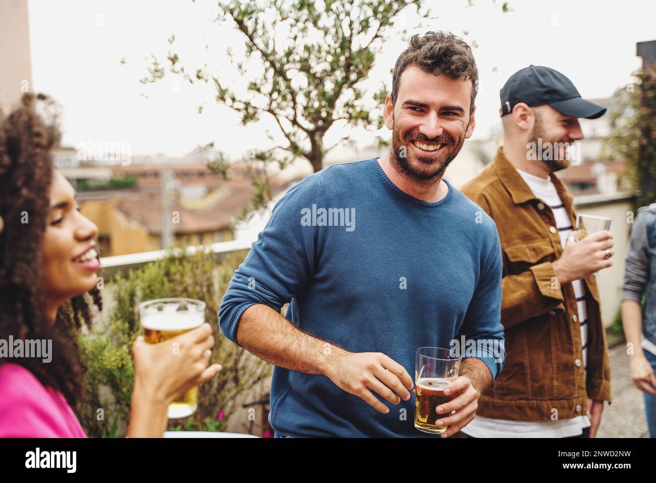 Gruppo di giovani studenti provenienti da diversi paesi che festeggiano insieme sulla terrazza. Un giovane con un bicchiere di birra sorride a una donna brasiliana mentre gli altri Foto Stock