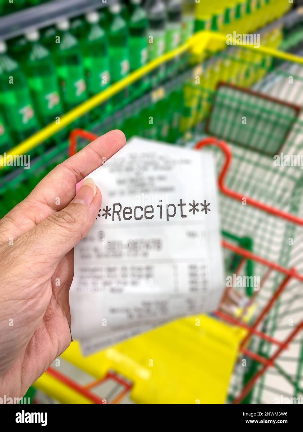 Tenere la mano e mostrare una ricevuta della drogheria con il carrello del supermercato sullo sfondo. Spese di shopping e concetto di inflazione. Foto Stock
