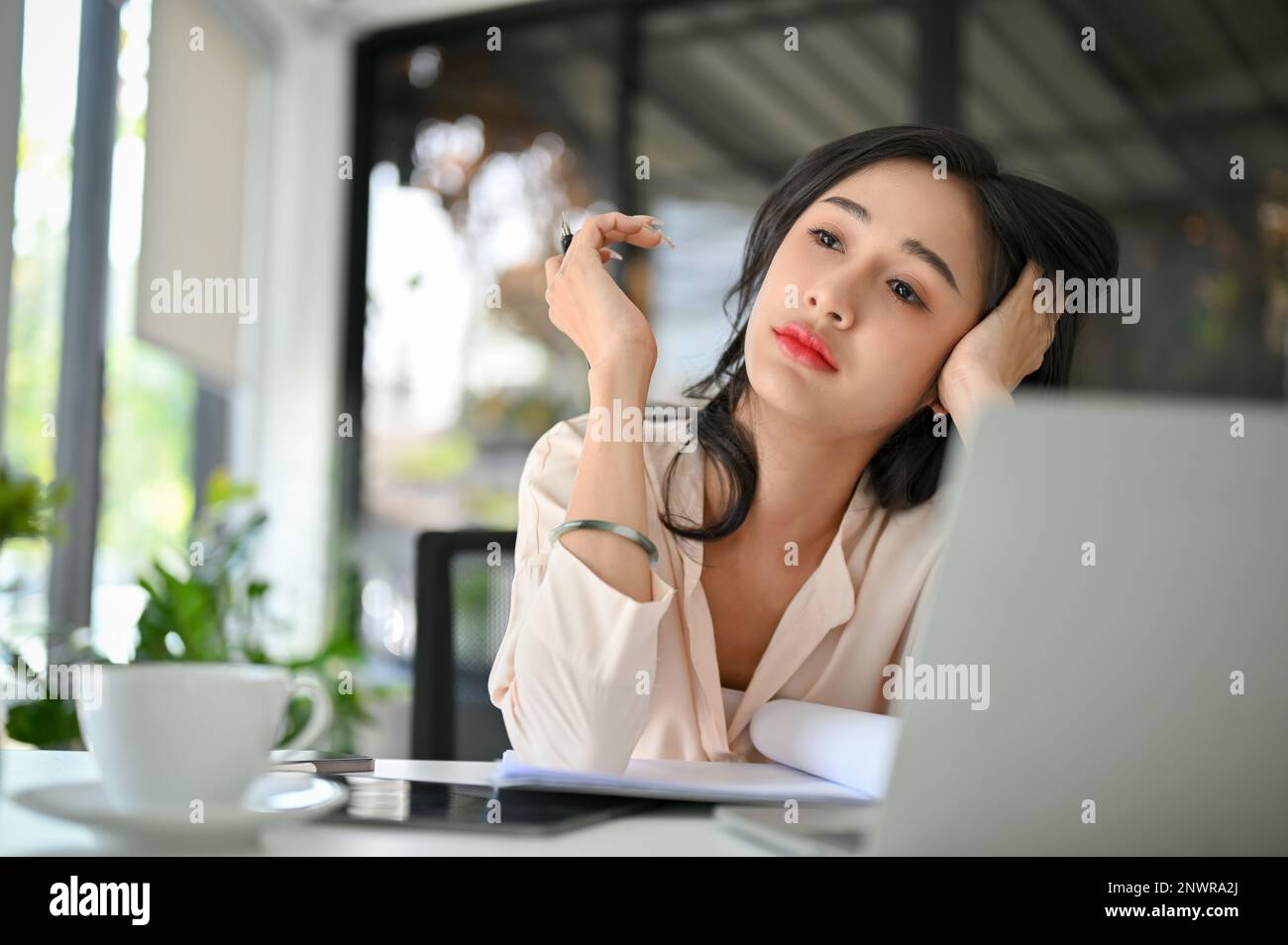 Lavorava troppo e stanca donna d'affari asiatica millenaria annoiata e stressata, lavorando alla sua scrivania in ufficio, mancanza di energia, mancanza di sonno. Foto Stock