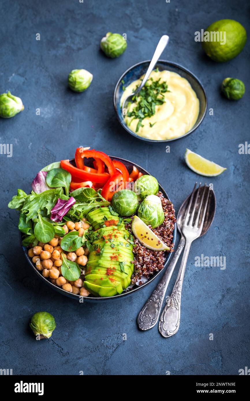 Ciotola con insalata sana e tuffo. Primo piano. Ciotola di Buddha con ceci, avocado, semi di quinoa, peperone rosso, spinaci freschi, germoglio di bruxelles, calce Foto Stock