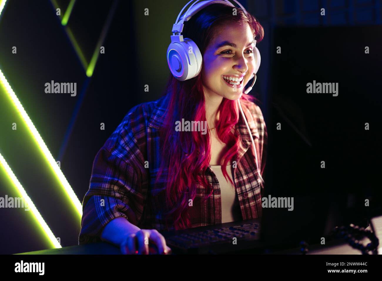 Giocatore femminile che domina un gioco per giocatore singolo online, navigando sapientemente nel mondo virtuale su un computer. Felice giovane donna sorridente come lei gioca un vid Foto Stock