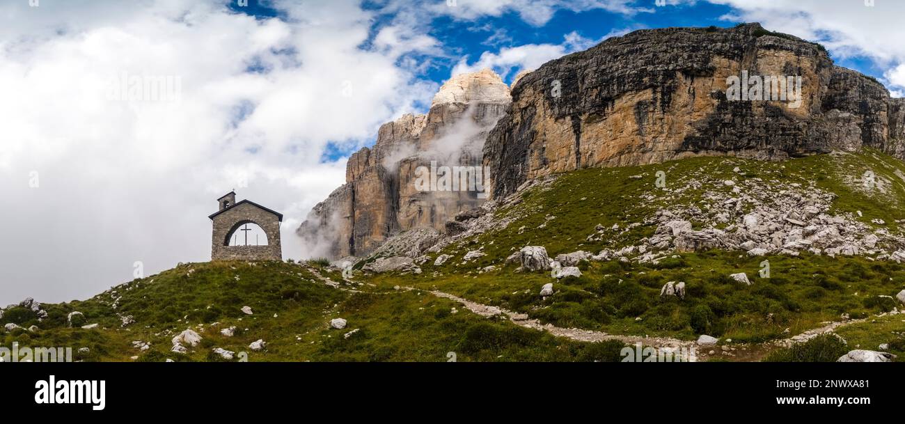 Vista panoramica della piccola cappella vicino al rifugio Maria e Alberto al Brentei nelle Dolomiti di Brenta, cime e scogliere rocciose in distan Foto Stock