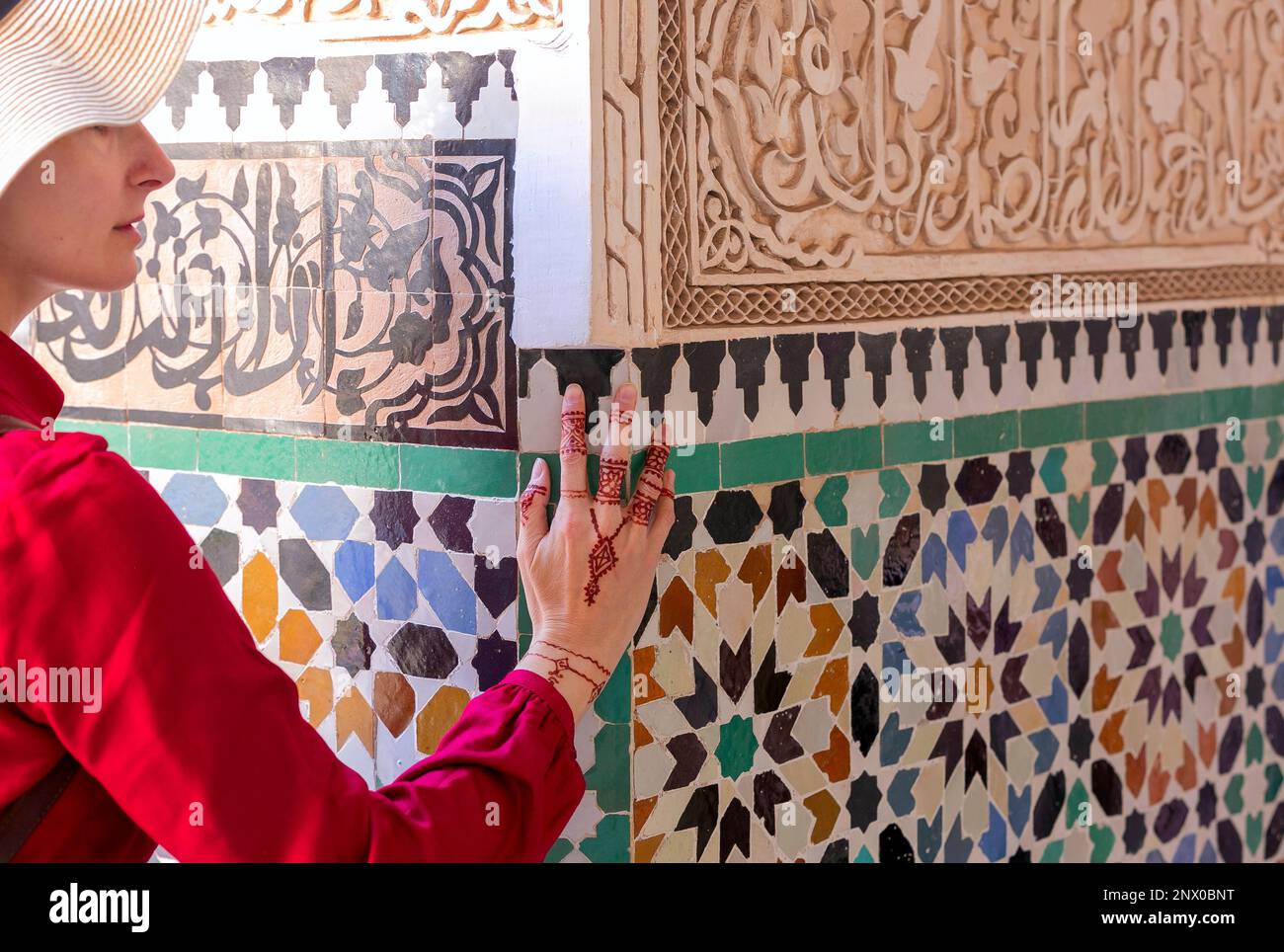 Donna in abito rosso che tocca parete in ceramica con motivo floreale a mano in henné pittura in marrakesc, marocco Foto Stock