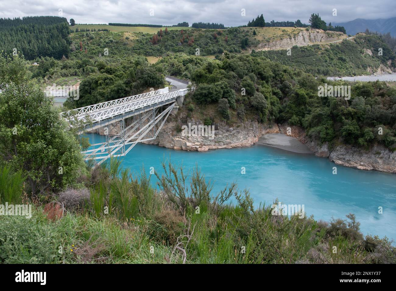 Le vibranti acque blu della gola del fiume Rakaia in Nuova Zelanda mentre le acque fluiscono sotto un ponte bianco. Foto Stock