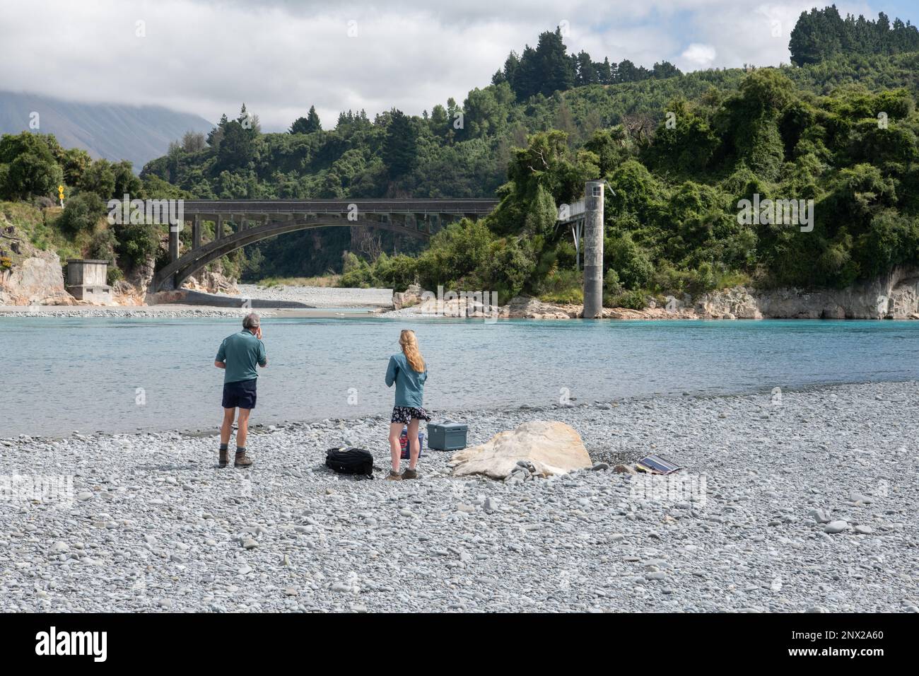 I turisti guardano il ponte sul fiume Rakaia e si trovano sulla riva del fiume di fronte al paesaggio panoramico della Nuova Zelanda. Foto Stock