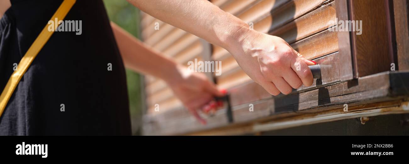 Le mani femminili tengono le maniglie del fermo di legno aprono le tende di legno all'aperto closeup Foto Stock