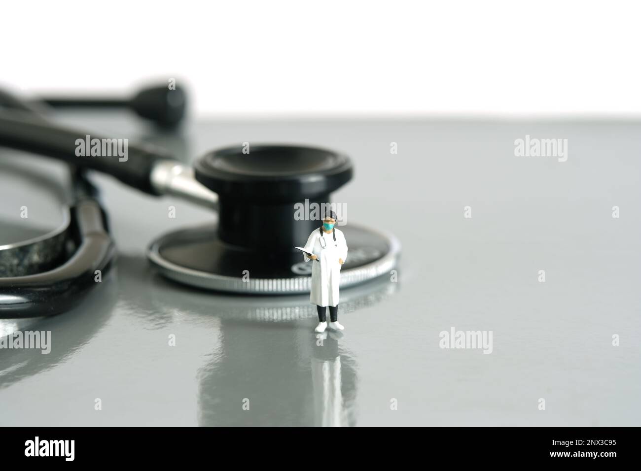 Fotografia di figura giocattolo delle persone in miniatura. Concetto di salute. Un medico di donne mentre sta in piedi con stetoscopio su una scrivania. Sfondo bianco isolato. PH immagine Foto Stock