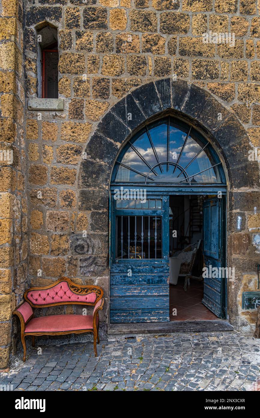 Antica porta medievale con un arco a punta dipinto di blu e una poltrona rosa accanto ad essa. Tuscania, provincia di viterbo, lazio, italia, europa Foto Stock