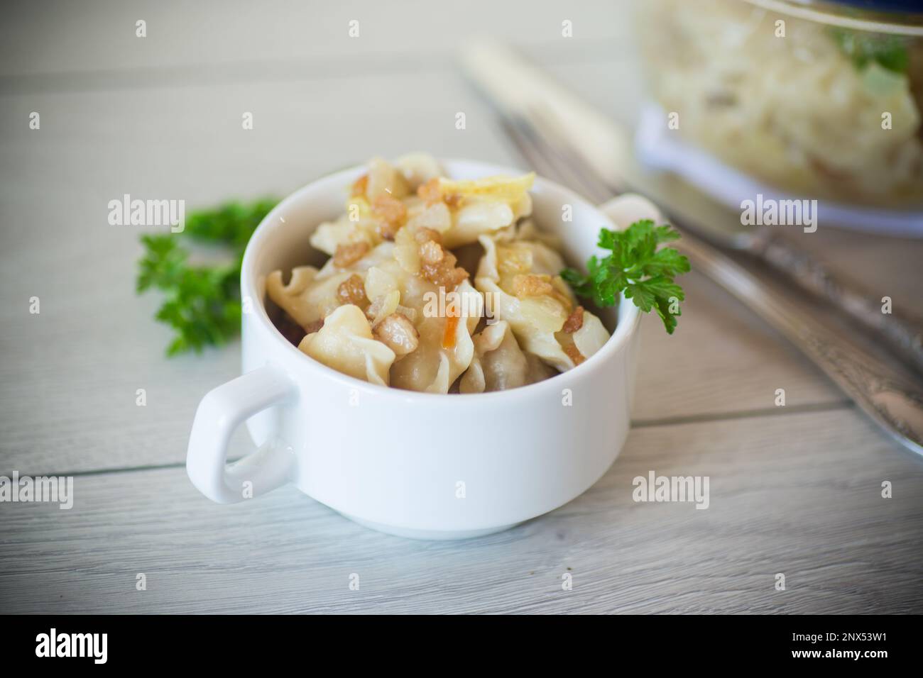 gnocchi cotti con patate e cipolle fritte, in una ciotola su un tavolo di legno. Foto Stock