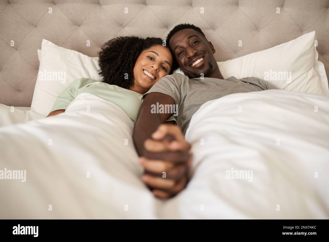 Giovane coppia multirazziale sorridente sdraiata a letto e tenuta le mani Foto Stock