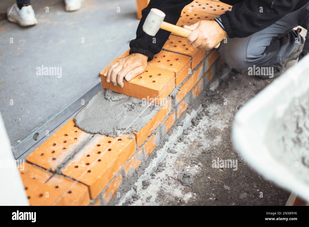 handyman martellando il mattone sul muro per attaccarlo Foto Stock