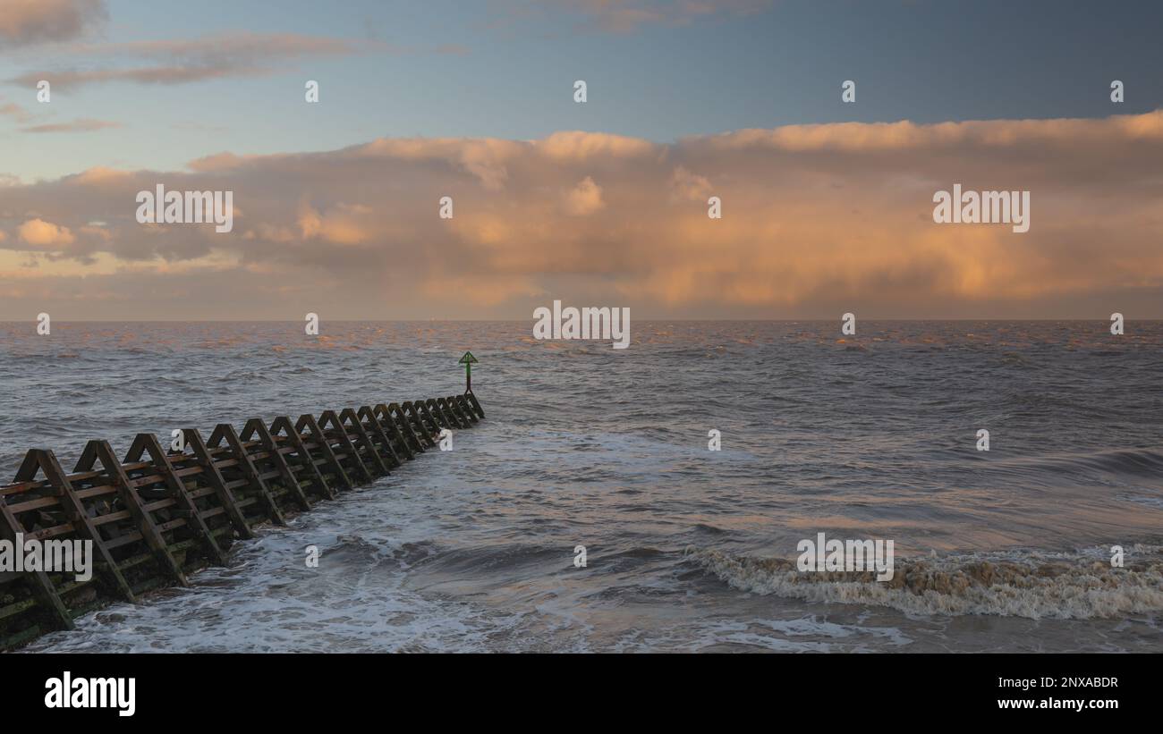 Walton al tramonto di Naze. Vista sugli interruttori a onde. Toni caldi del sole. Le onde si schiantano. Giorno ventoso. Foto Stock