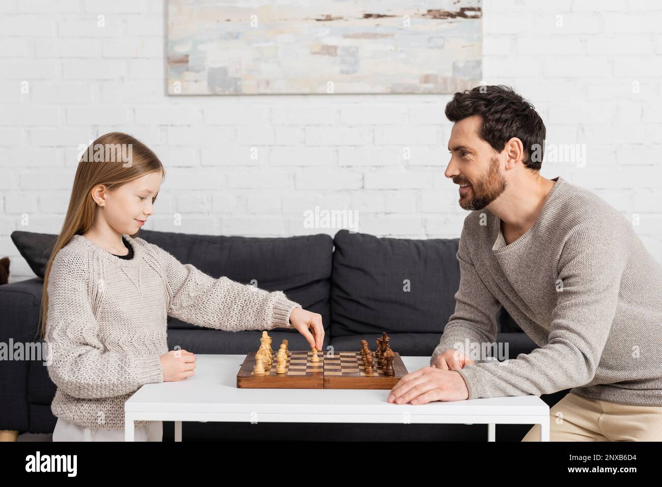 vista laterale di ragazza intelligente che gioca a scacchi con padre allegro in soggiorno, immagine stock Foto Stock