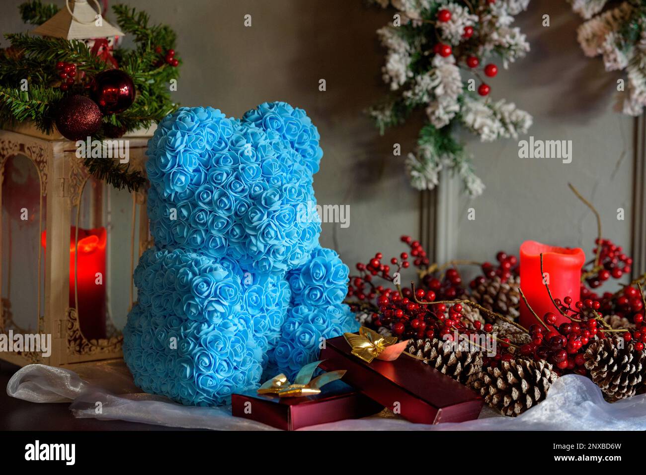 Primo piano di un orsacchiotto blu fatto di rose su un tavolo accanto a decorazioni natalizie assortite Foto Stock