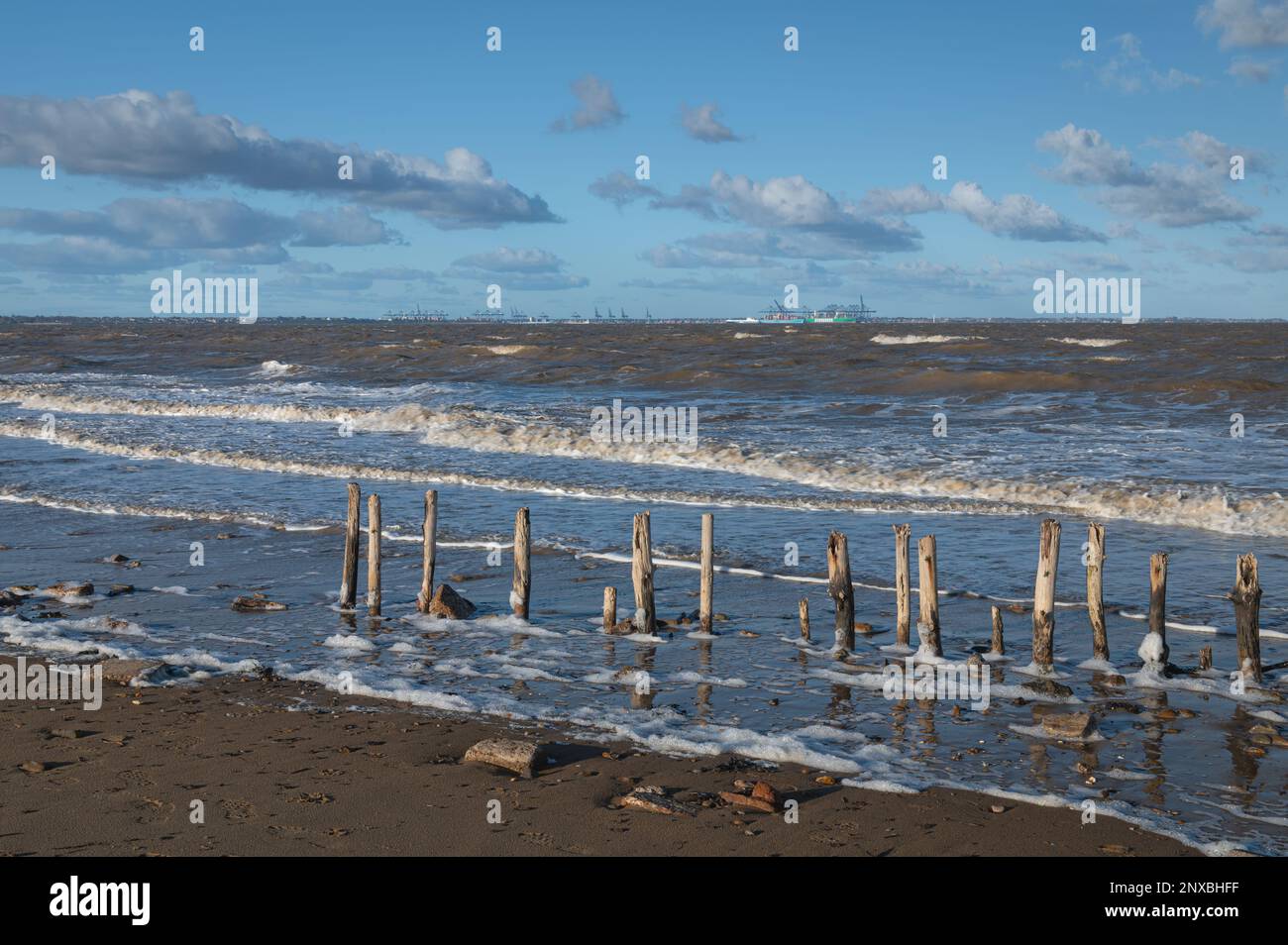 Pali di legno su una spiaggia a Walton sulla Naze in Essex. Paesaggio invernale. Le onde si schiantano. Giorno ventoso. Foto Stock