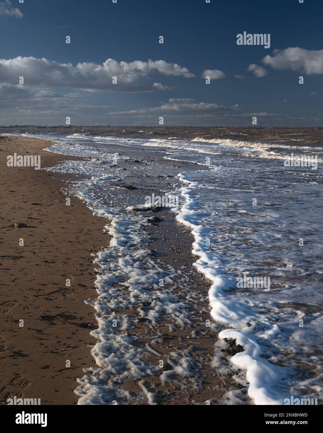 Onde e modelli di onde su una spiaggia di Walton sul Naze in Essex. Giorno ventoso. Schiuma sulla sabbia. Foto Stock