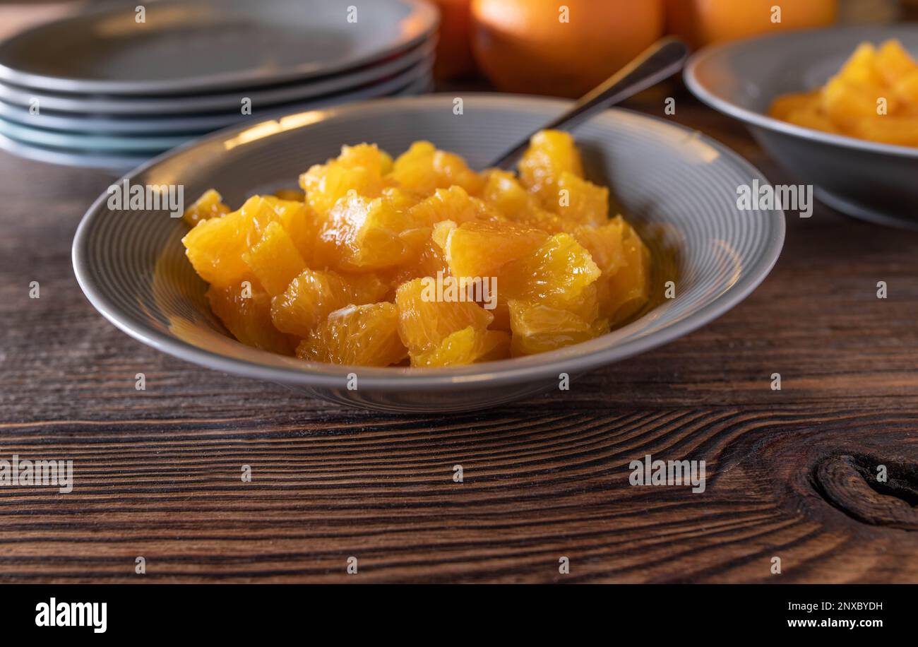 Arance tritate in una ciotola con cucchiaio per dessert o snack su tavola di legno. Primo piano, vista frontale con spazio per le copie Foto Stock