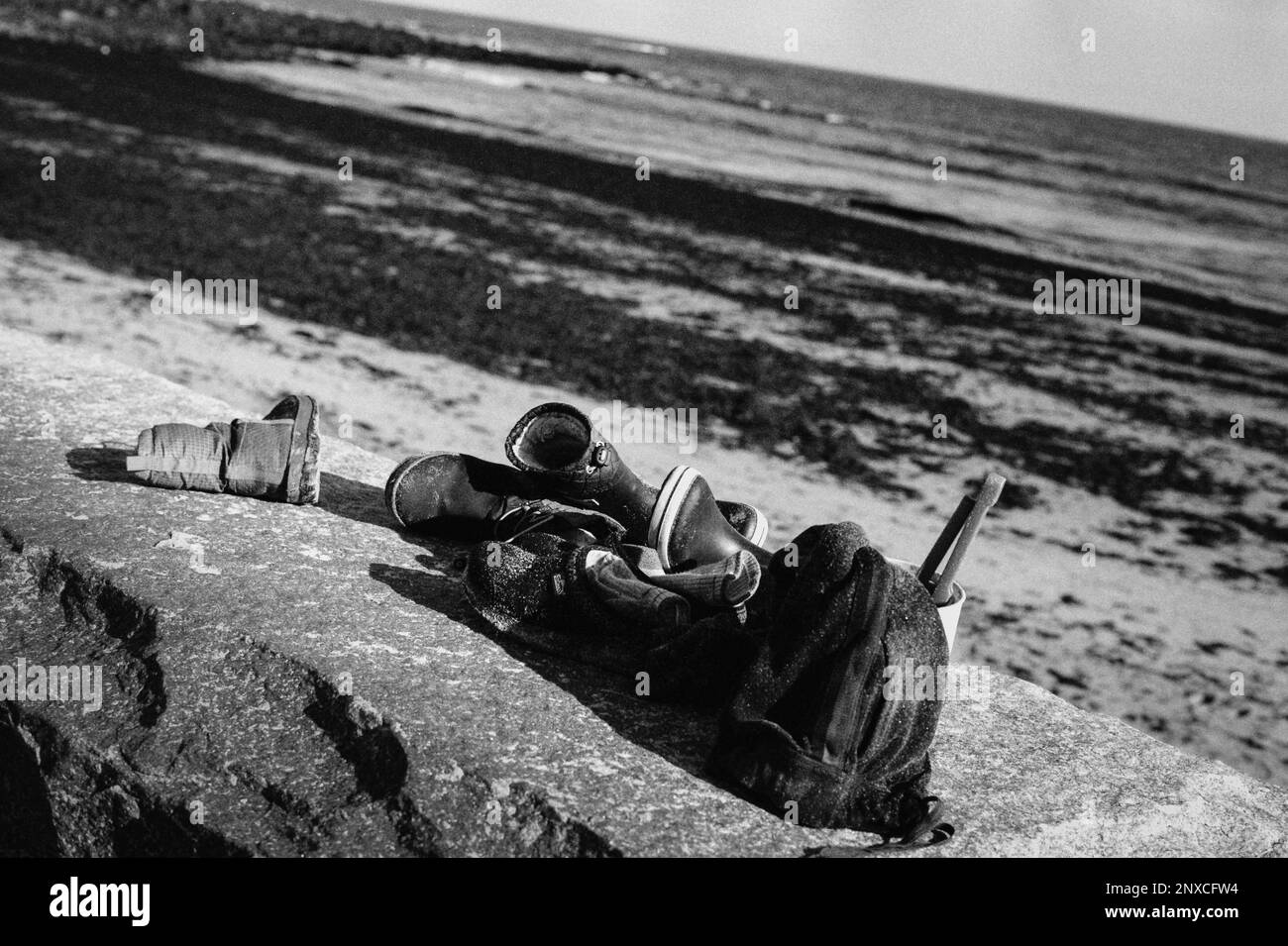Stivali, confezioni e giocattoli per bambini impilati su un muro di pietra accanto alla spiaggia sabbiosa in un giorno d'autunno a North Hampton Beach, New Hampshire. L'immagine era Foto Stock