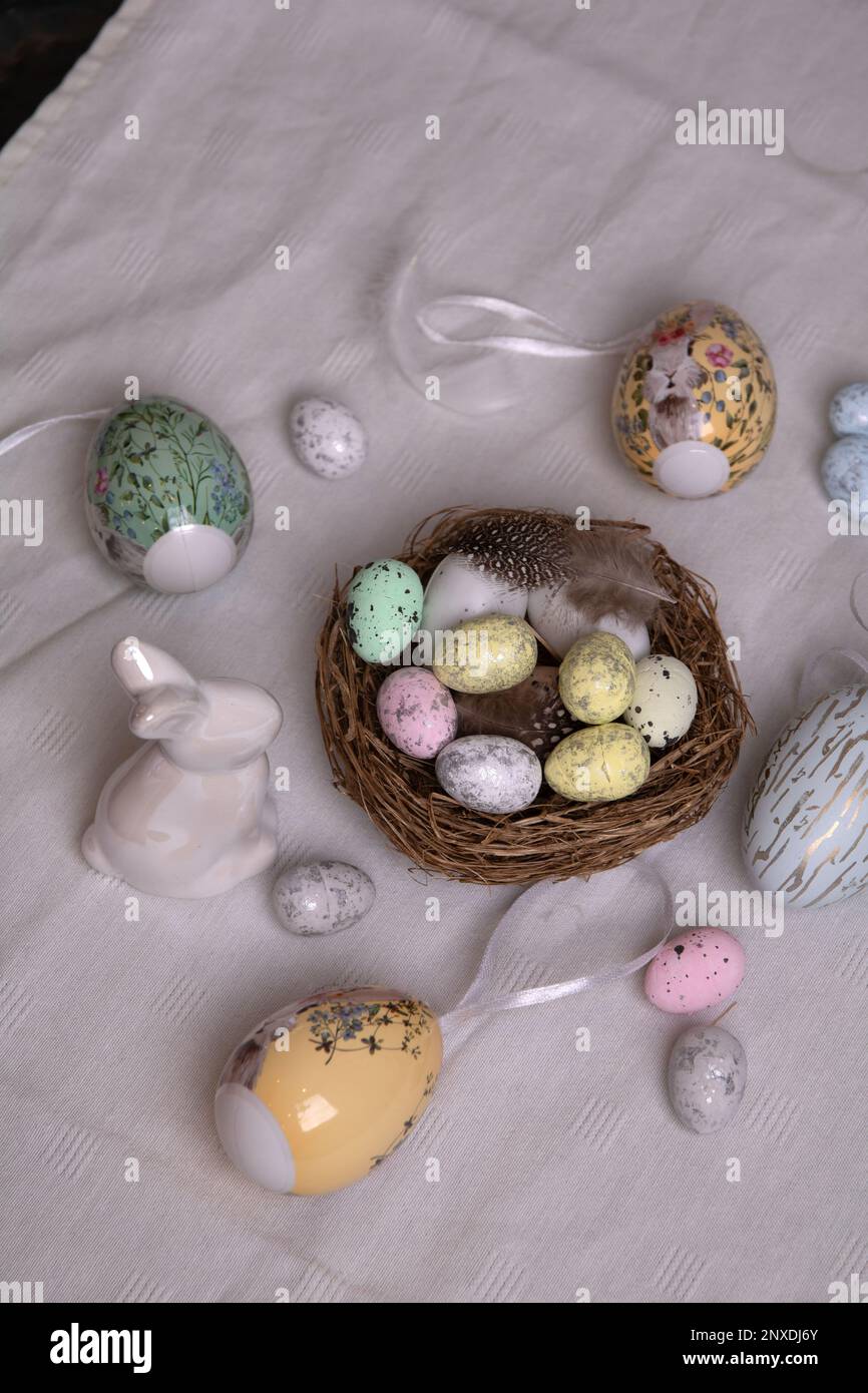 Foto su una tovaglia bianca con un sacco di uova decorative e un uovo bianco di coniglietto di Pasqua e un nido di uova di quaglia colorate sul tavolo Foto Stock