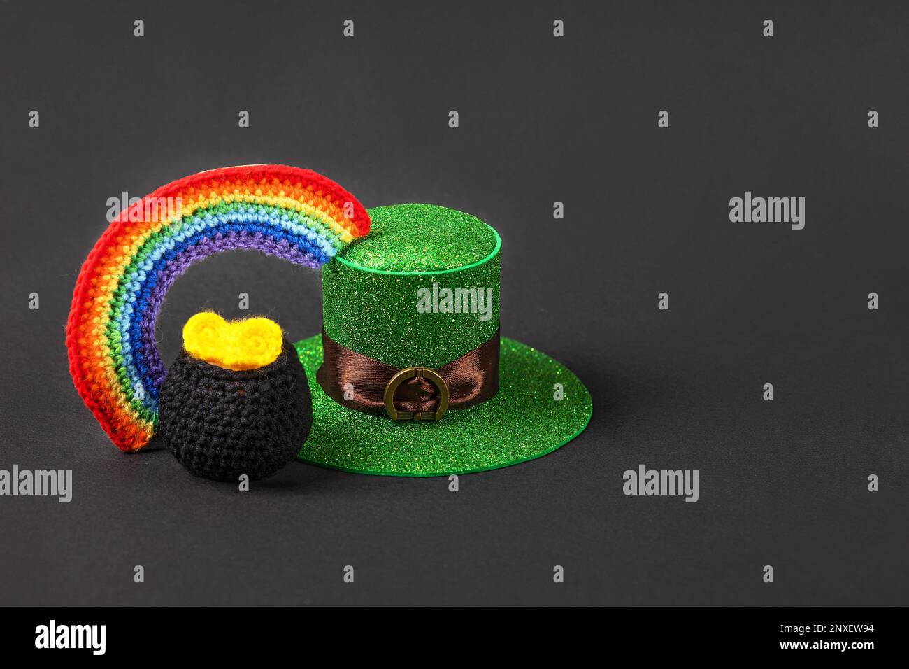 Concetto del giorno di San Patrizio. Composizione di un cappello verde, calderone nero lavorato a maglia con monete e un arcobaleno luminoso a sette colori su sfondo nero. Post Foto Stock