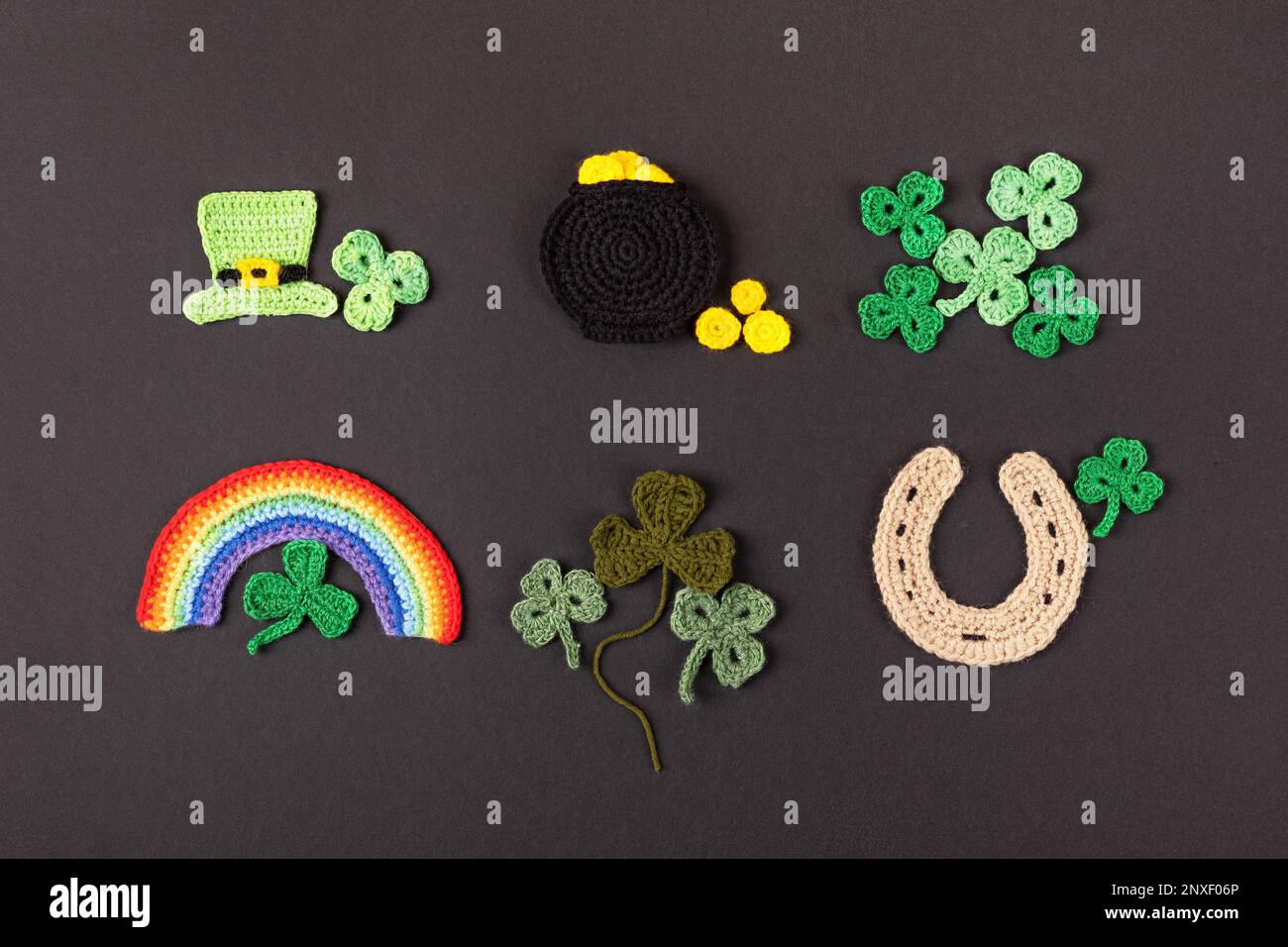 Concetto del giorno di San Patrizio. Composizione a maglia di un cappello verde, una pentola d'oro, un ferro di cavallo, un arcobaleno e shamrock verde su sfondo nero Foto Stock