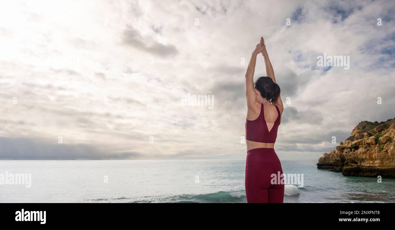 Donna in piedi presso l'oceano con le braccia sollevate meditando, concetto di spazio di testa. Foto Stock