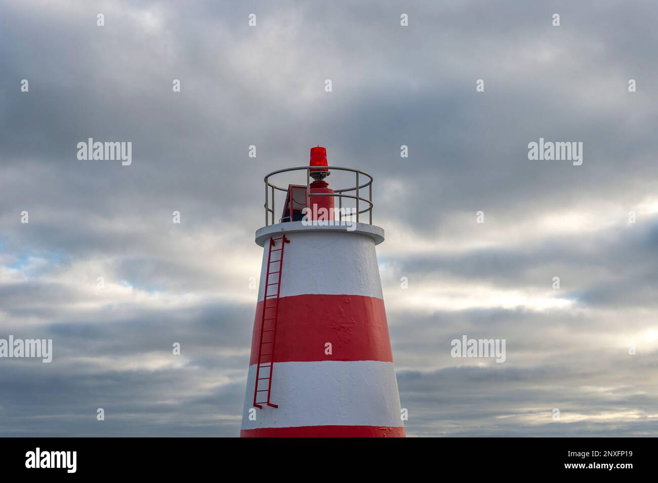 Top of a red and white lighthouse beacon against a cloudy sky. Foto Stock