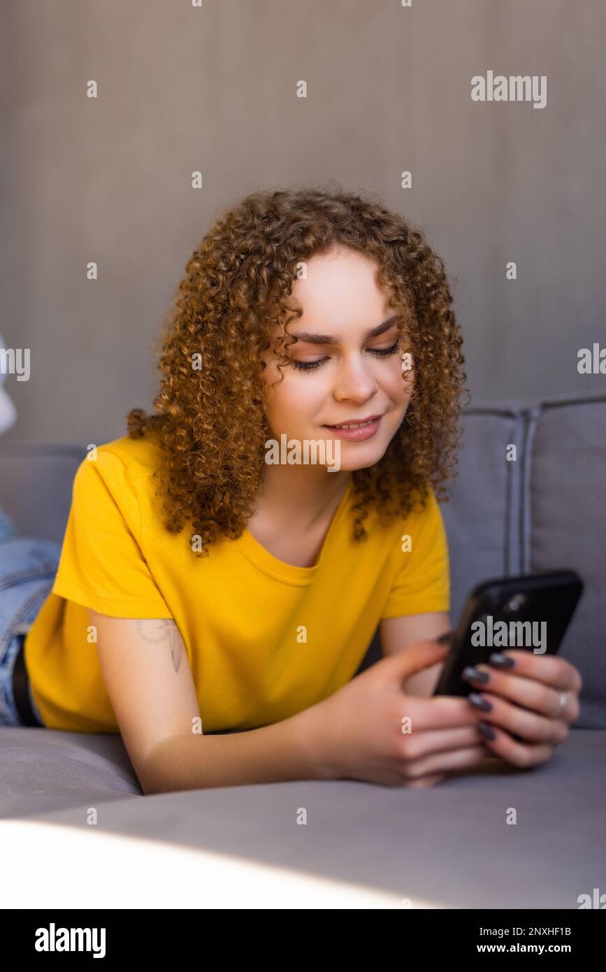 Calma donna attraente sedersi sul divano utilizzando smartphone, primo piano. Generazione e tecnologia moderna uso quotidiano per divertimento, fare ordine a distanza, comunicazione r Foto Stock