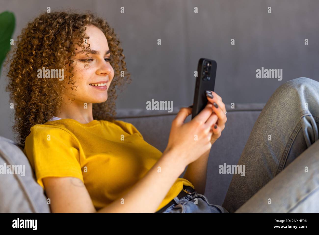 Calma donna attraente sedersi sul divano utilizzando smartphone, primo piano. Generazione e tecnologia moderna uso quotidiano per divertimento, fare ordine a distanza, comunicazione r Foto Stock