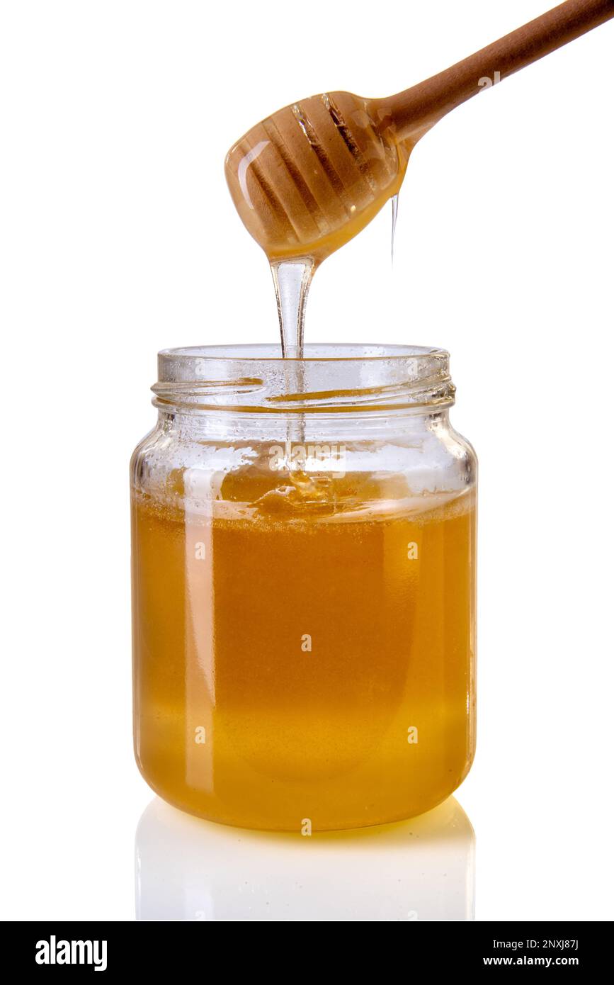 Miele che sgocciola dal tuffatore del miele di legno in vaso di vetro, miele di acacia isolato su bianco con il percorso di clipping Foto Stock