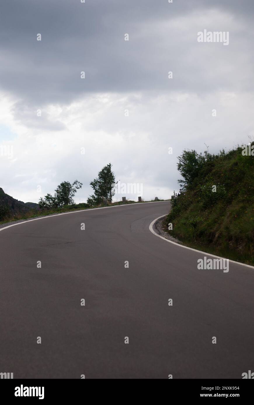 Vista sulla strada di montagna vicino a verdi colline in condizioni climatiche nuvolose nelle Alpi Foto Stock