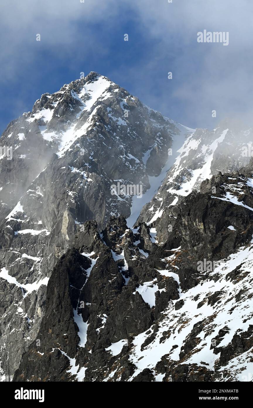 Vista panoramica della catena montuosa di Vysoké Tatry con neve, nuvole nebbiose e cielo blu sopra Tatranská Lomnica con la vetta del Kežmarský štít Foto Stock