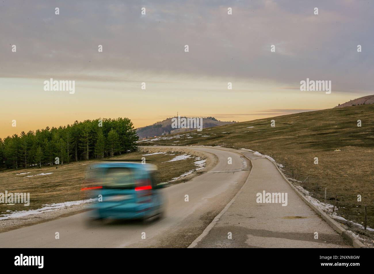 Una macchina sfocata gira sulla strada con una foresta sullo sfondo Foto Stock