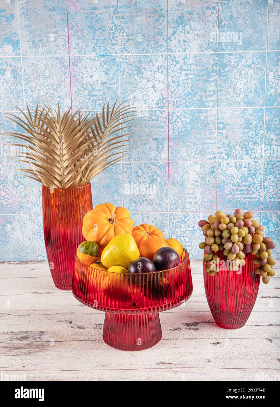 Zucca ornamentale, frutta e uva in vaso. Porta frutta vaso in vetro colorato. Decanter in vetro rosso con coperchio rimosso. Foto Stock