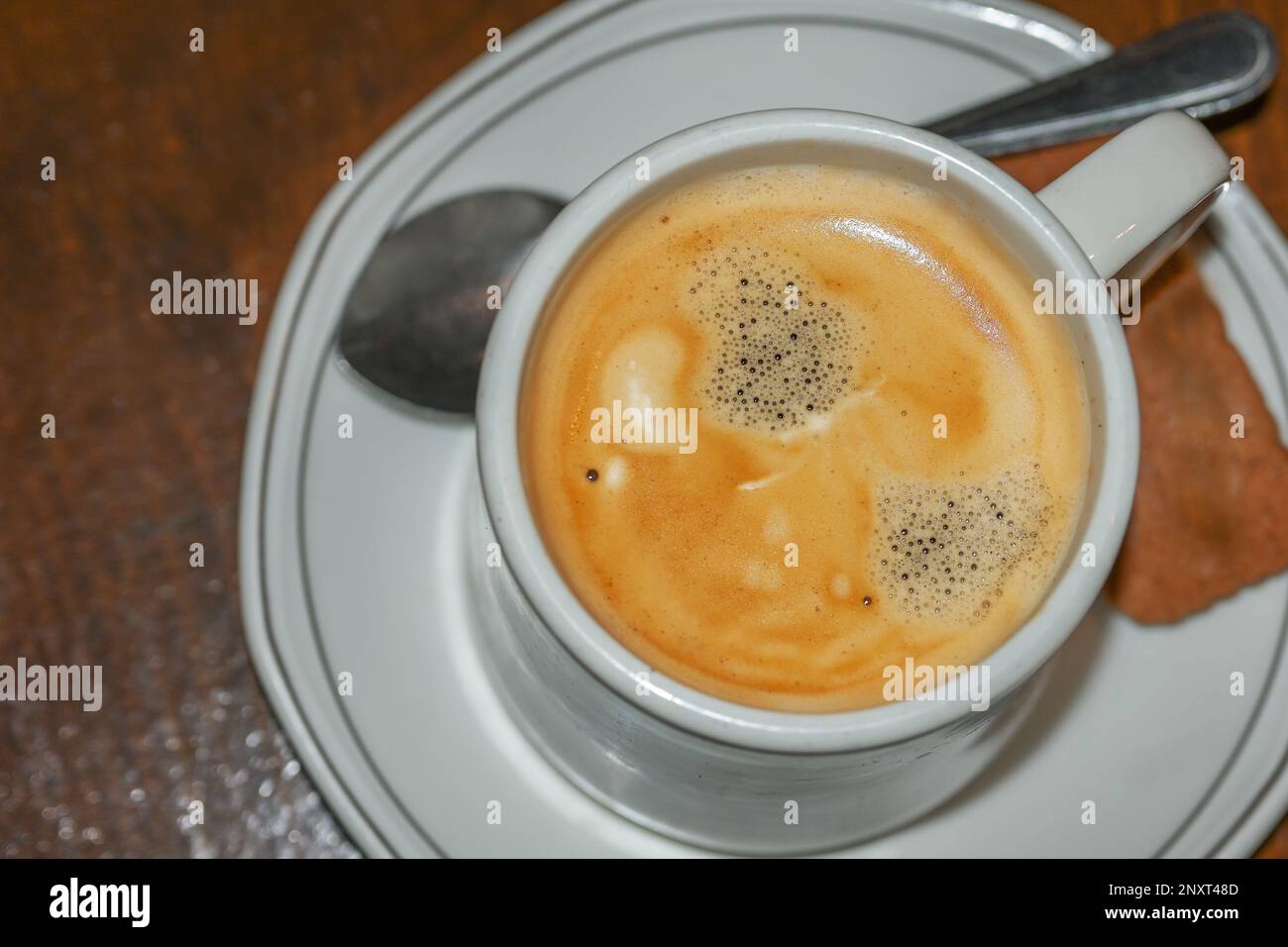 Crema di caffè appena preparata in una tazza bianca con biscotti e cucchiaio su un tavolo di legno, vista dall'alto, spazio copia, messa a fuoco selezionata, profondità molto ridotta di Foto Stock