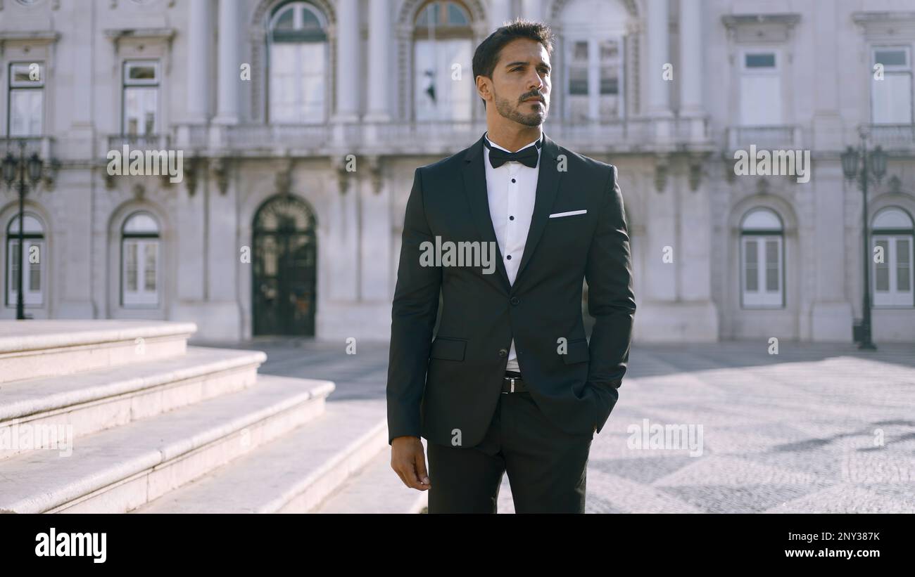 Elegante uomo in tuta si erge sulla strada della città europea. Azione. Uomo attraente in tuta elegante nelle giornate di sole. Uomo di sogni che abito. Foto Stock