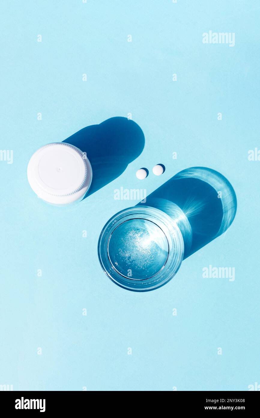 Pillole e bicchiere d'acqua su sfondo blu. Medicina, concetto di assistenza sanitaria. Foto Stock