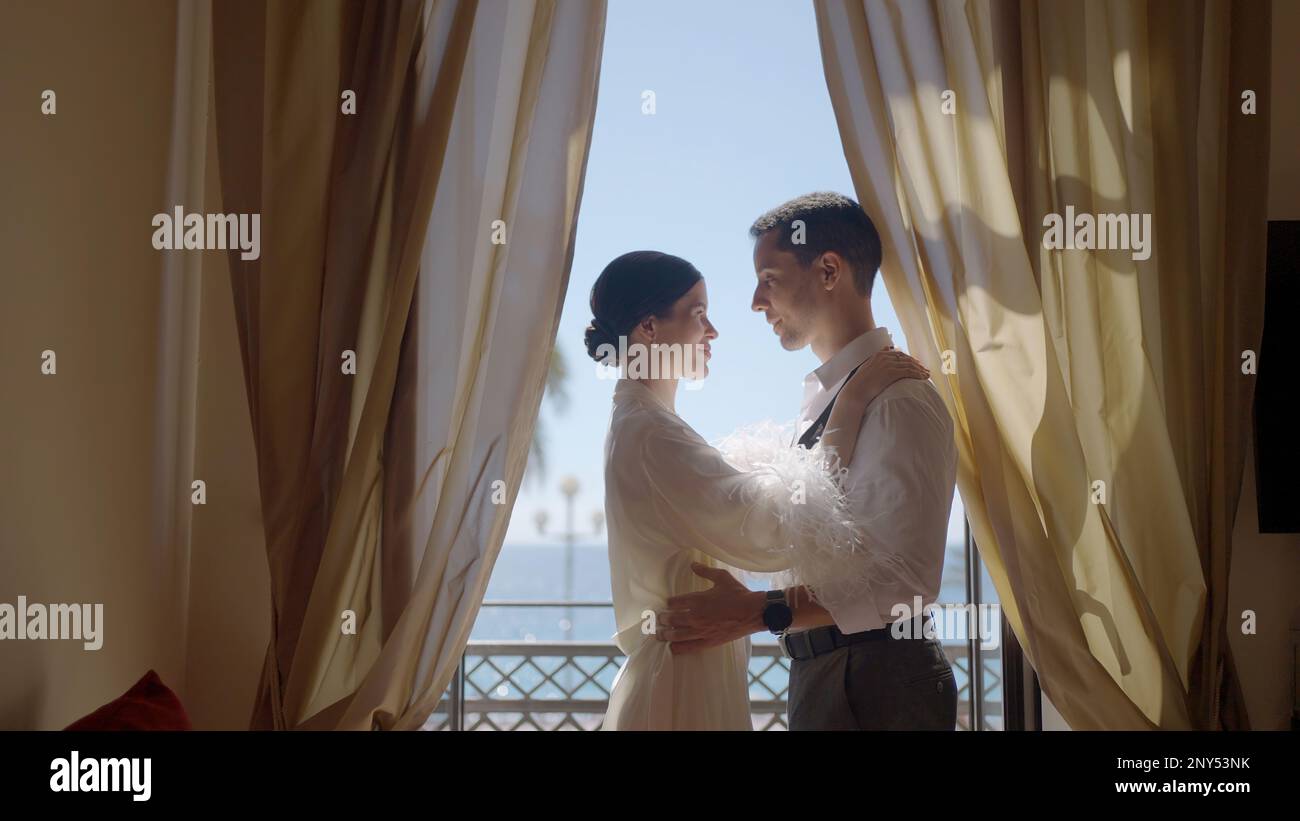 Coppia carina che posa sullo sfondo delle finestre dell'appartamento. Azione. Un giovane uomo con la sua ragazza in un appuntamento a casa con la luce brillante Foto Stock