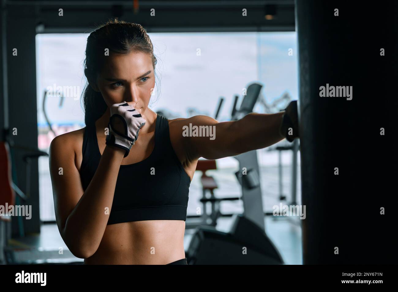 Giovane donna che pratica boxe in palestra, indossa guanti da boxe e colpisce un sacchetto da punzonatura. Foto Stock