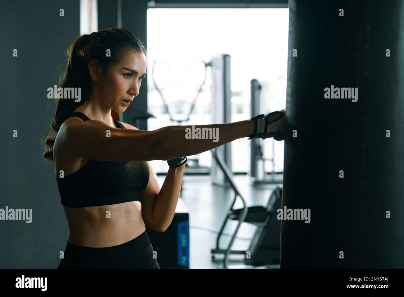 Giovane donna che pratica boxe in palestra, indossa guanti da boxe e colpisce un sacchetto da punzonatura. Foto Stock