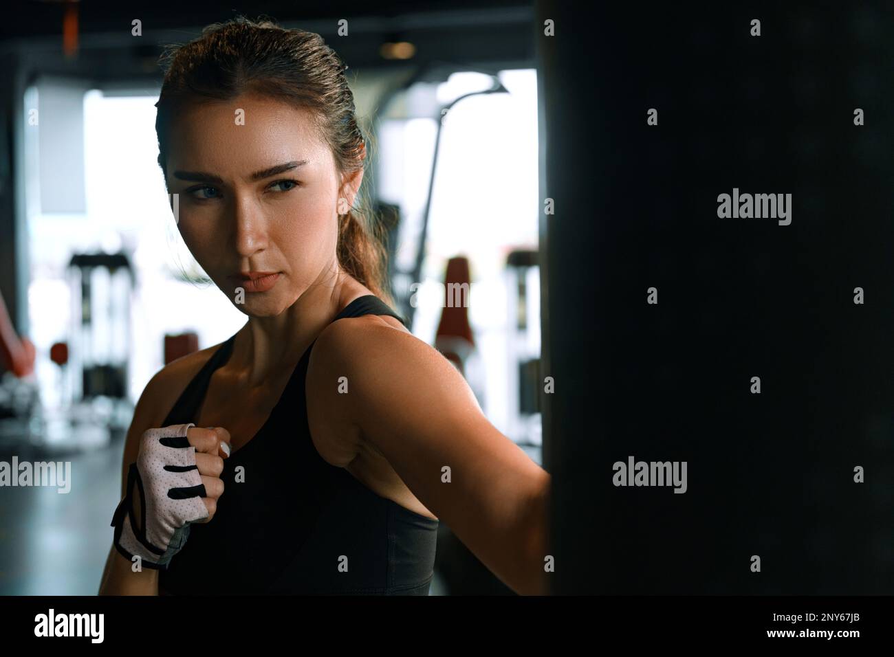 Giovane donna che pratica boxe in palestra, indossa guanti da boxe e colpisce un sacchetto da punzonatura. Foto Stock