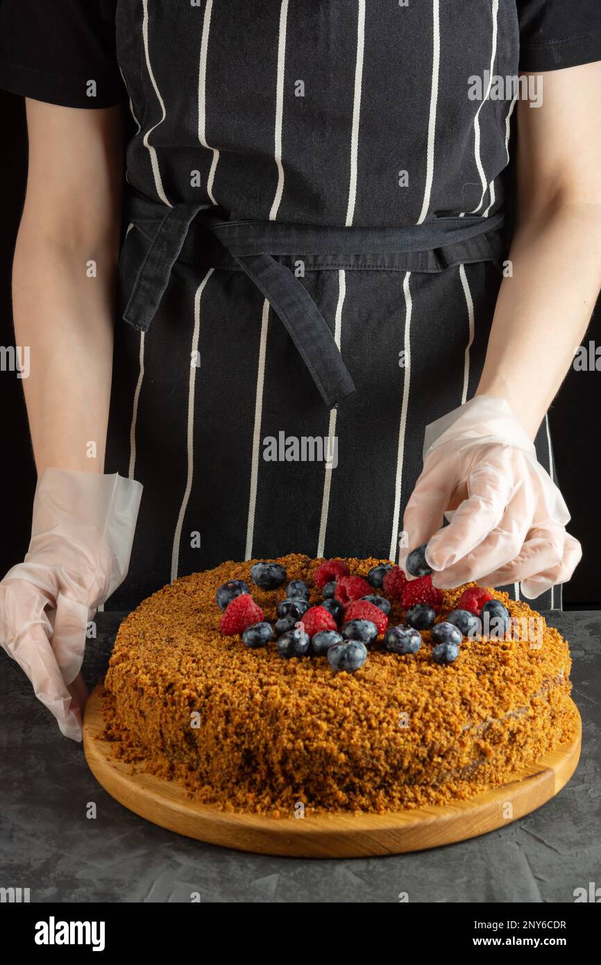 Uno chef femminile decora una torta di carote fatta in casa con frutti di bosco freschi su sfondo scuro. messa a fuoco selettiva Foto Stock