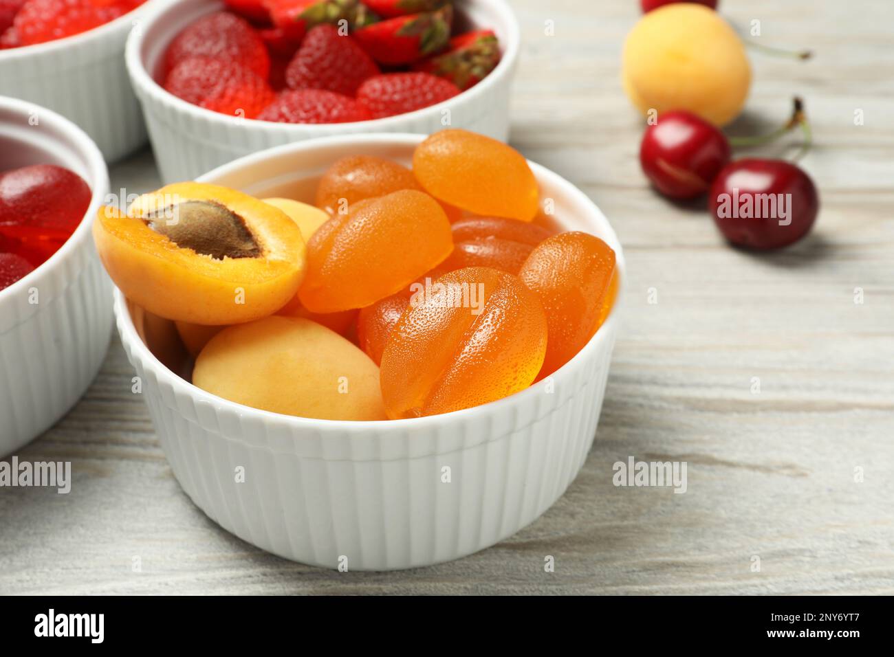 Deliziose caramelle gommose e frutta fresca su tavola di legno bianco, primo piano Foto Stock