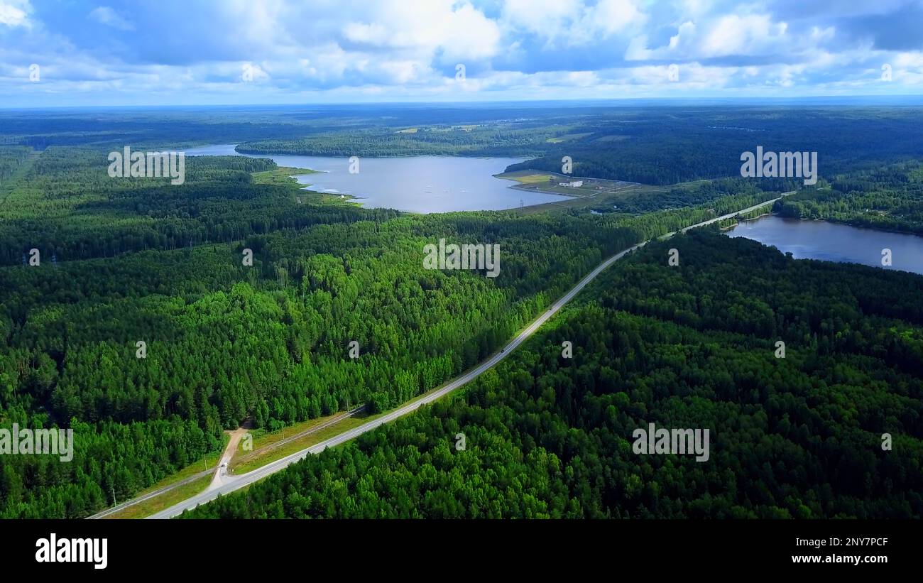 Veduta aerea di una strada stretta che diventa un ponte sopra il lungo fiume. Fermo. Verde foresta e cielo nuvoloso blu Foto Stock