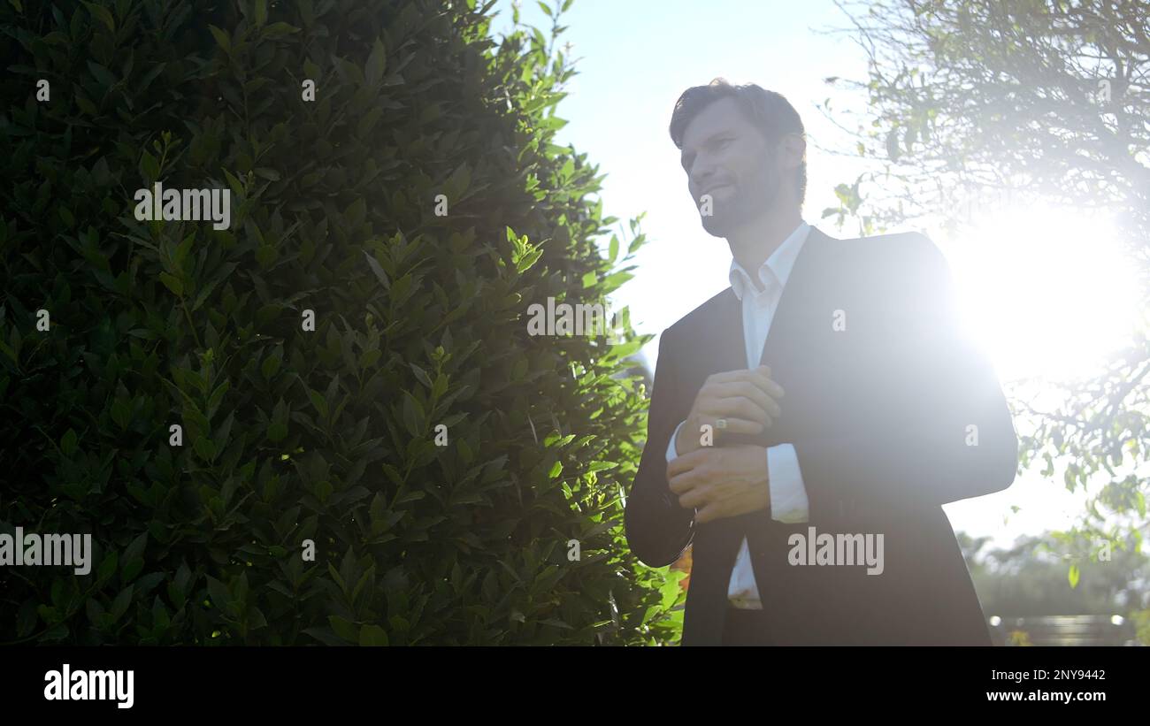 Un uomo cammina nel parco. Azione. Sole splendente attraverso foglie verdi di alberi e cespugli Foto Stock