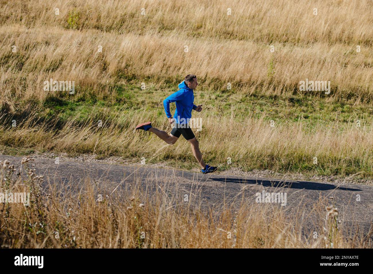 corridore maschio che corre su strada in campo di erba secca Foto Stock