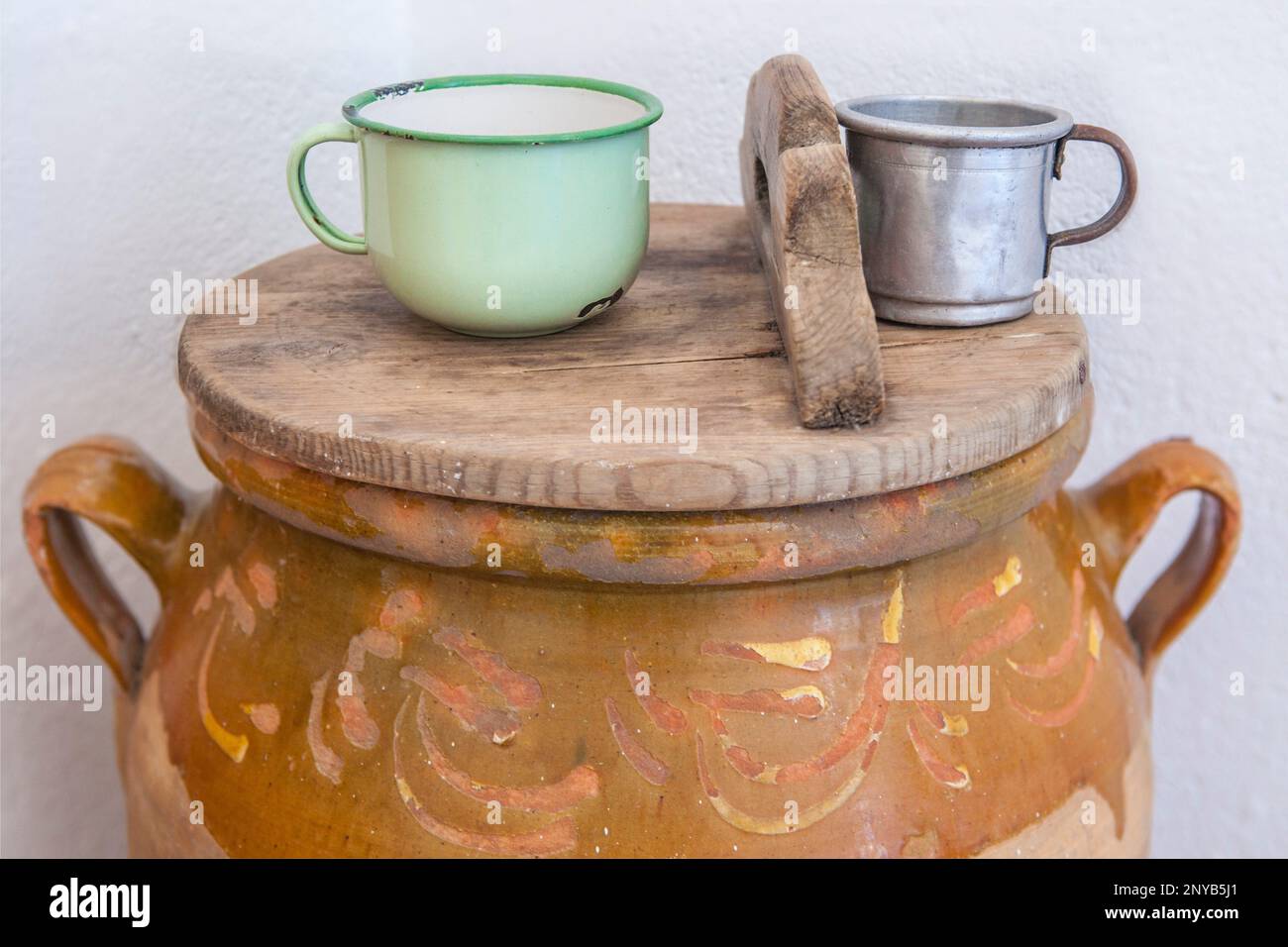 Grande vaso di terracotta con coperchio e tazze per acqua potabile. Vecchio concetto di cucina Cottage. Foto Stock