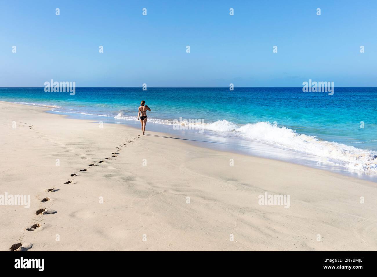 Donna turistica in costume da bagno a piedi su una spiaggia di sabbia idilliaca in una giornata di sole estate sull'isola di SAL, Cabo Verde Foto Stock