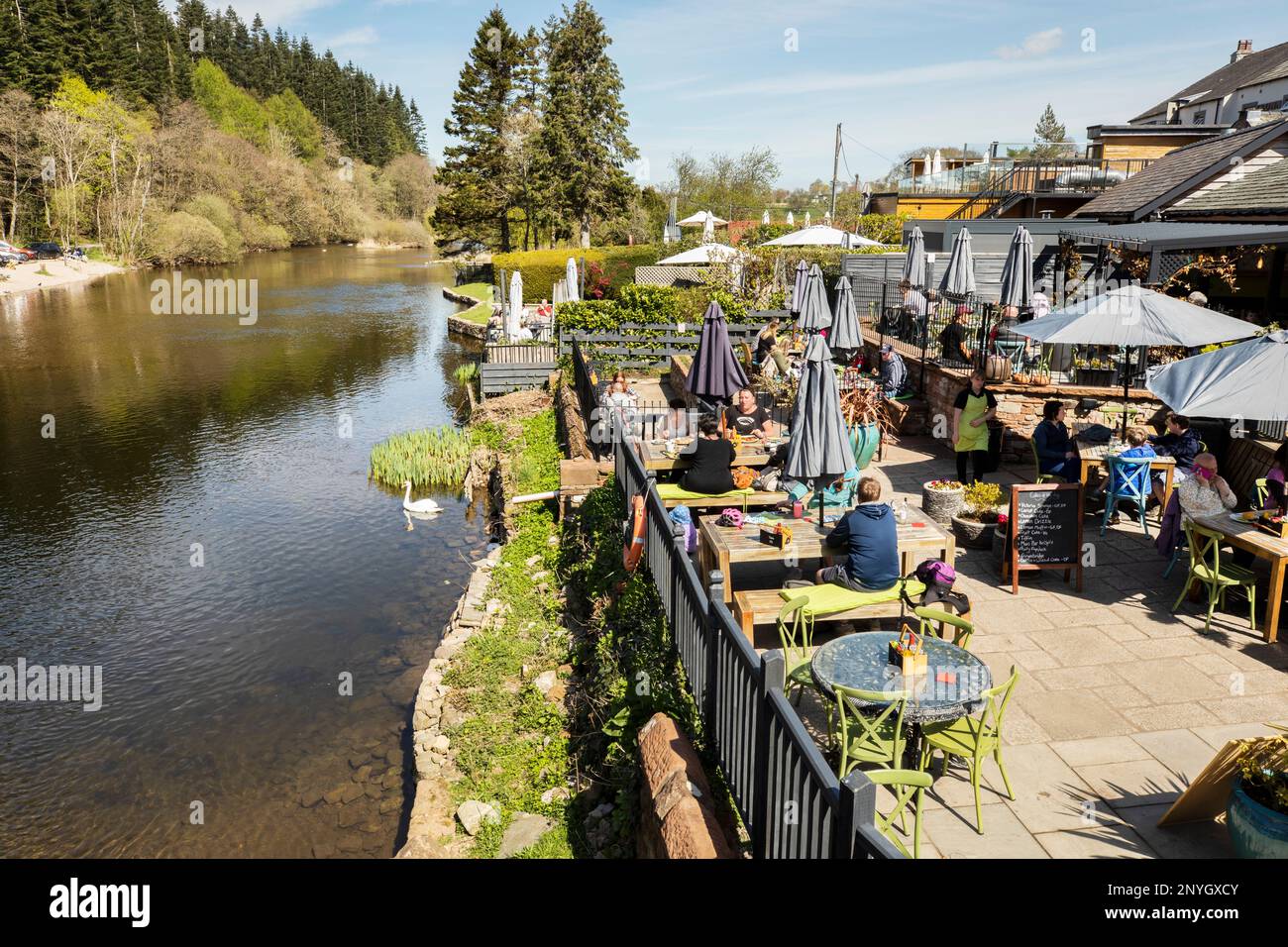 Un affollato caffè e sala da tè accanto al fiume Eamont con i turisti che mangiano all'aperto godendosi il sole al Pooley Bridge Ullswater Lake District, Cumbria Foto Stock