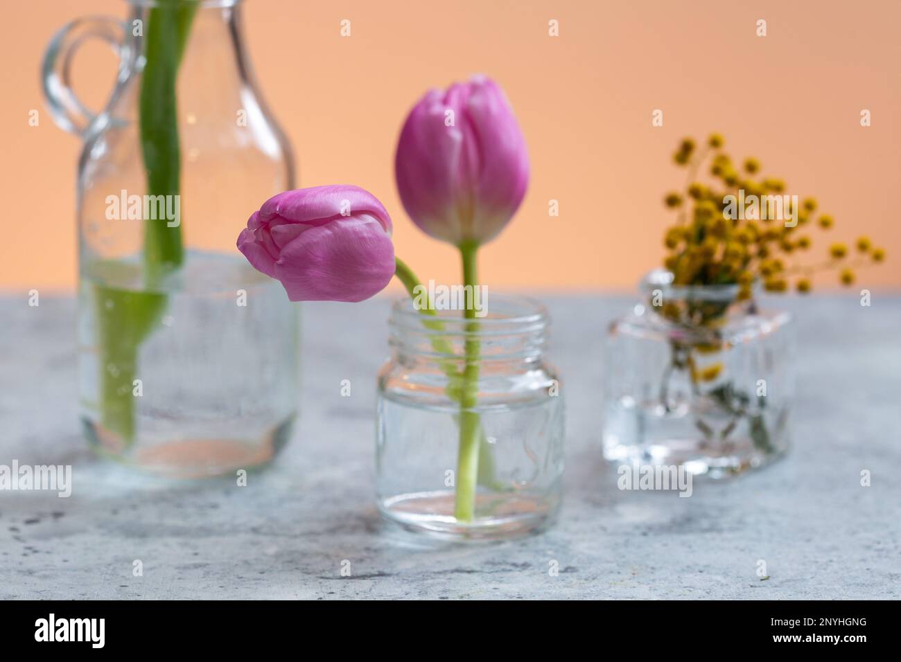 I tre vasi di vetro trasparente su un tavolo con fiori vari Foto Stock